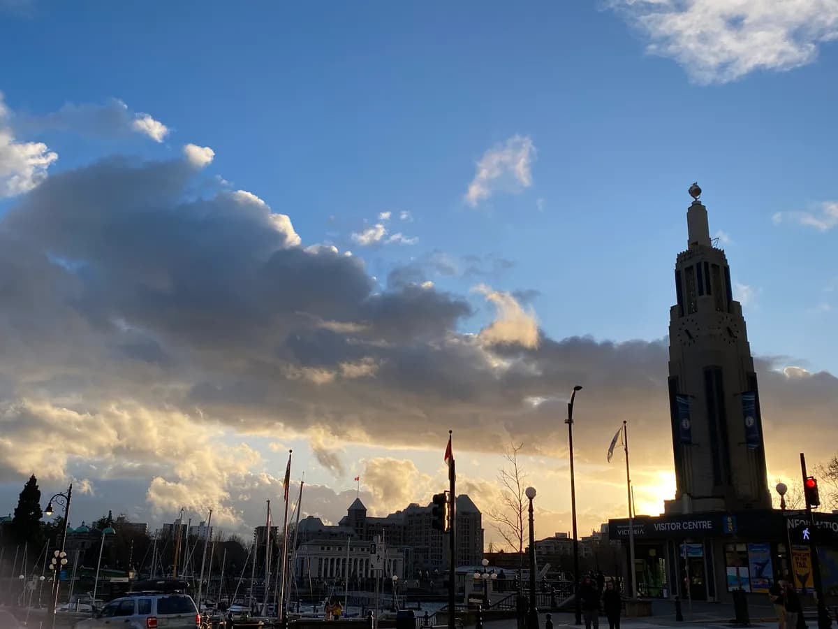 Victoria, BC Inner Harbour at sunset with the Visitor Centre clock tower and marina silhouetted against dramatic clouds